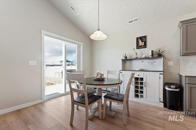 dining area with vaulted ceiling, a textured ceiling, and light hardwood / wood-style flooring