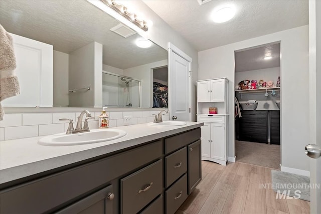 bathroom with walk in shower, a textured ceiling, vanity, hardwood / wood-style flooring, and decorative backsplash