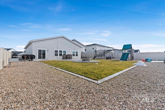 rear view of property featuring a trampoline, a yard, a patio, and a playground