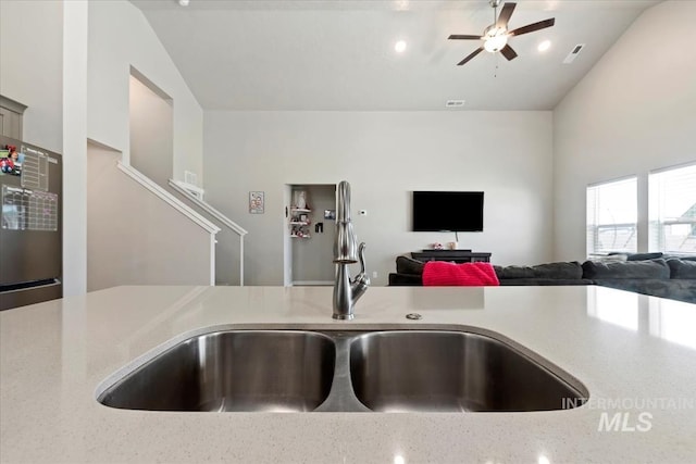 kitchen with vaulted ceiling, sink, fridge, ceiling fan, and light stone counters