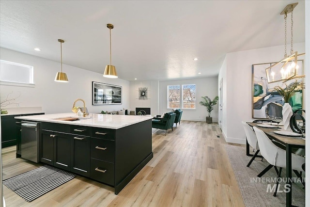 kitchen with dishwasher, sink, an island with sink, decorative light fixtures, and light wood-type flooring