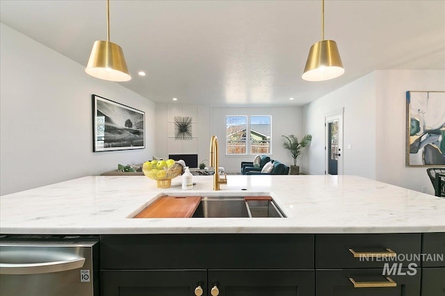 kitchen with light stone counters, sink, an island with sink, and hanging light fixtures