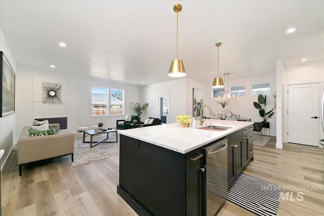 kitchen featuring light stone countertops, sink, light hardwood / wood-style flooring, an island with sink, and pendant lighting