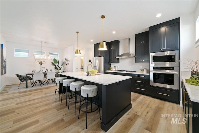 kitchen featuring wall chimney exhaust hood, a breakfast bar, stainless steel appliances, pendant lighting, and a center island with sink