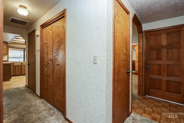 hallway featuring visible vents, a textured ceiling, and a textured wall