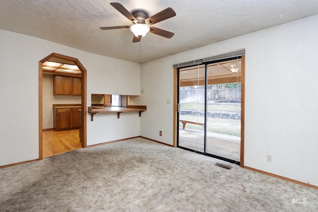 unfurnished living room with carpet, a ceiling fan, visible vents, arched walkways, and a textured ceiling