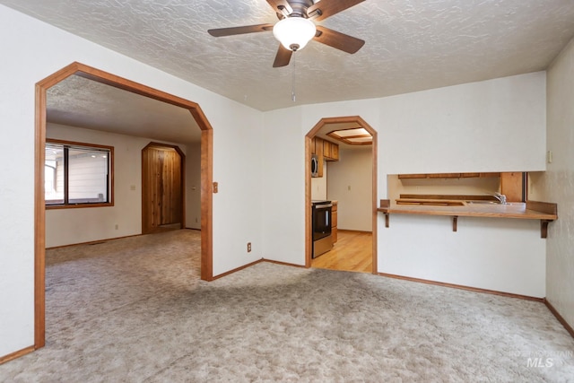 unfurnished living room with a sink, arched walkways, a textured ceiling, and light carpet