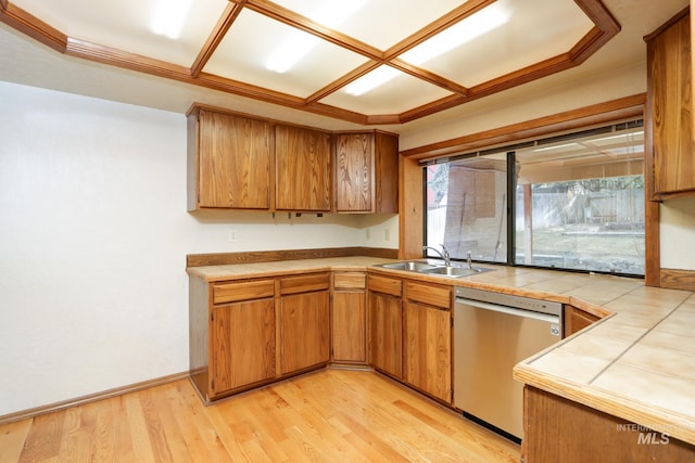 kitchen with brown cabinets, a sink, stainless steel dishwasher, light wood-style floors, and tile counters