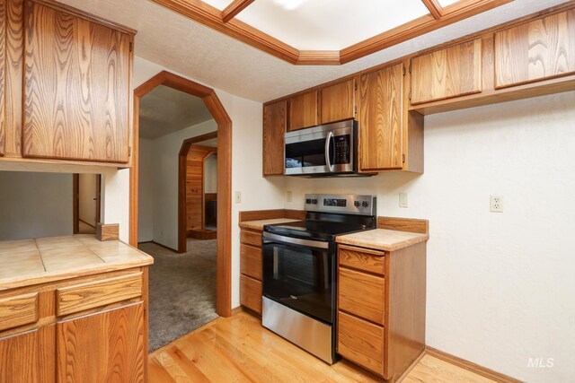 kitchen featuring brown cabinetry, tile countertops, light wood-type flooring, arched walkways, and stainless steel appliances