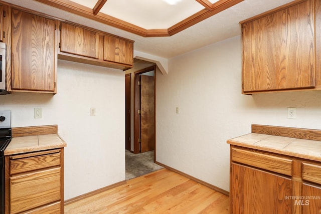 kitchen featuring light wood-style flooring, white microwave, brown cabinets, and tile countertops