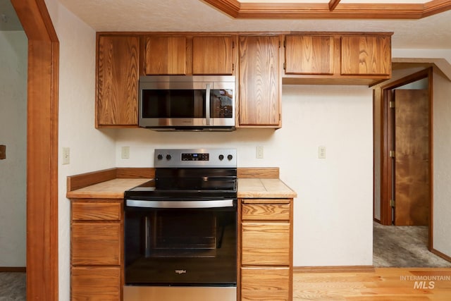 kitchen featuring range with electric stovetop, tile counters, a textured ceiling, stainless steel microwave, and brown cabinets