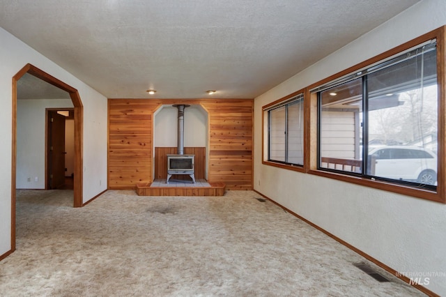 unfurnished living room with wooden walls, carpet, visible vents, a wood stove, and a textured ceiling