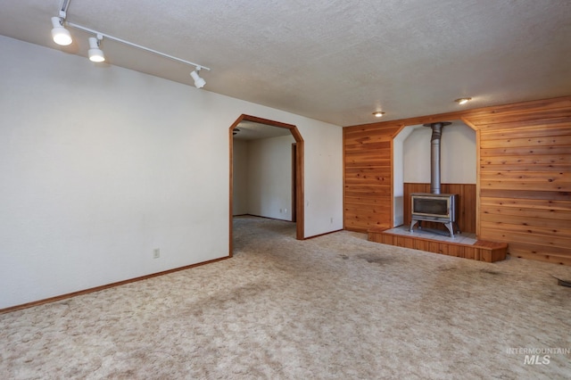 unfurnished living room with a wood stove, arched walkways, wood walls, a textured ceiling, and carpet flooring