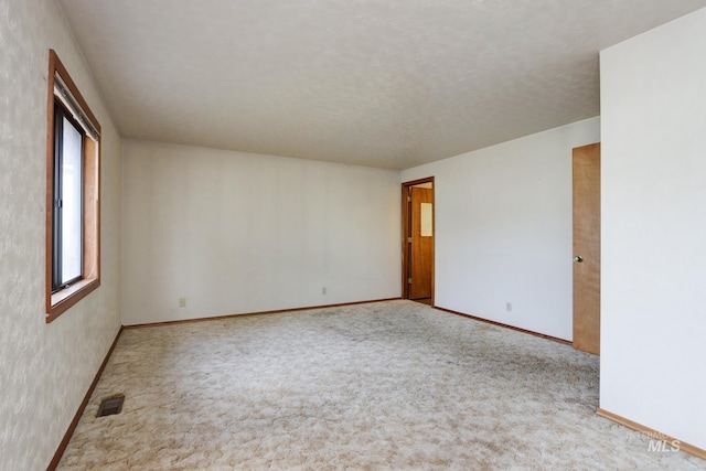 spare room featuring a textured ceiling, carpet, visible vents, and baseboards