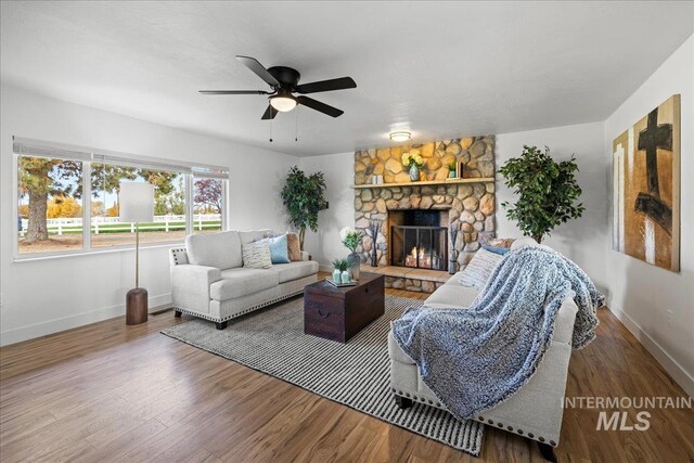living room featuring ceiling fan, wood-type flooring, and a stone fireplace