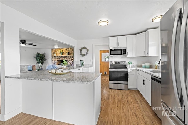 kitchen with light stone counters, kitchen peninsula, light hardwood / wood-style flooring, white cabinetry, and appliances with stainless steel finishes