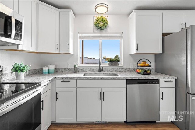 kitchen featuring dark wood-type flooring, sink, light stone countertops, white cabinetry, and appliances with stainless steel finishes
