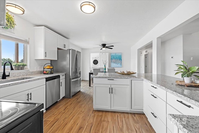 kitchen featuring stacked washer and clothes dryer, stainless steel appliances, white cabinetry, sink, and light hardwood / wood-style flooring