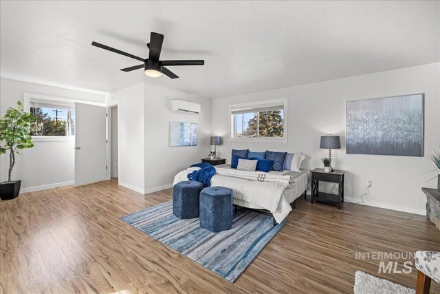 bedroom featuring hardwood / wood-style flooring, multiple windows, ceiling fan, and a wall mounted AC