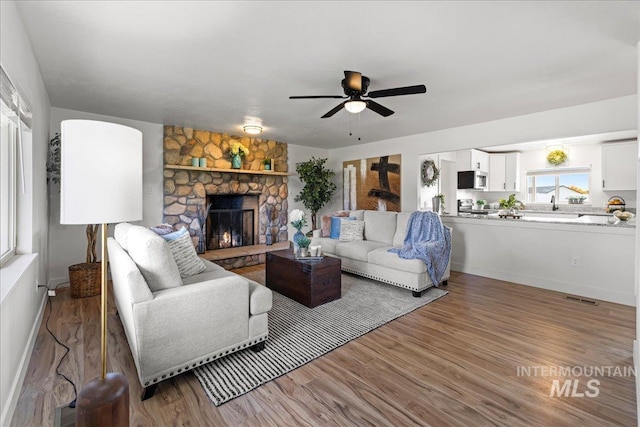 living room featuring hardwood / wood-style floors, a stone fireplace, and ceiling fan