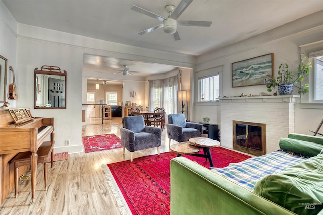 living area with a brick fireplace, wood finished floors, and ceiling fan