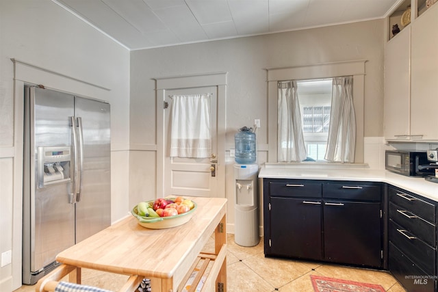 kitchen with black microwave, light countertops, light tile patterned floors, dark cabinetry, and stainless steel fridge