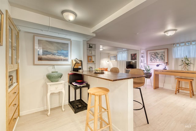 kitchen featuring built in shelves, baseboards, a peninsula, light wood-style floors, and a kitchen bar