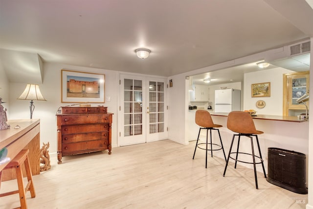 interior space featuring light wood-type flooring, french doors, a breakfast bar area, and freestanding refrigerator