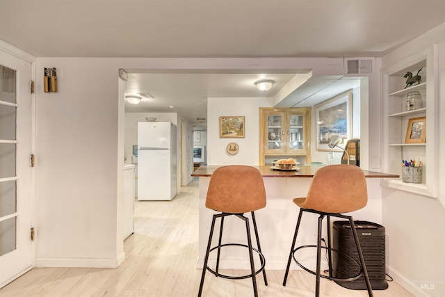 kitchen with visible vents, baseboards, freestanding refrigerator, light wood-style floors, and a kitchen breakfast bar