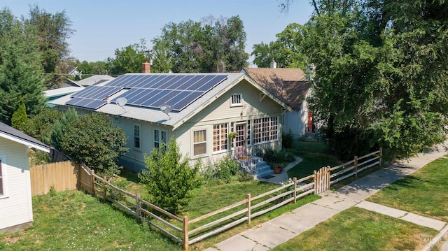 view of front facade featuring a front lawn, fence, and roof mounted solar panels