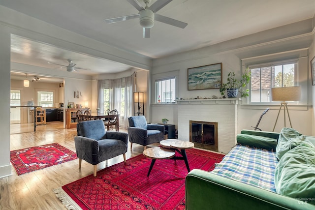 living area featuring a wealth of natural light, a brick fireplace, wood finished floors, and a ceiling fan