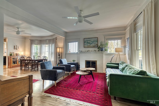 living area featuring a wealth of natural light, a brick fireplace, ceiling fan, and wood finished floors