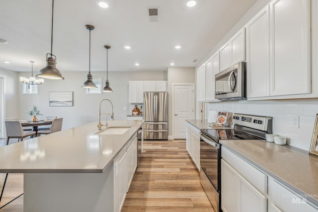 kitchen featuring a center island with sink, stainless steel appliances, hanging light fixtures, sink, and white cabinetry