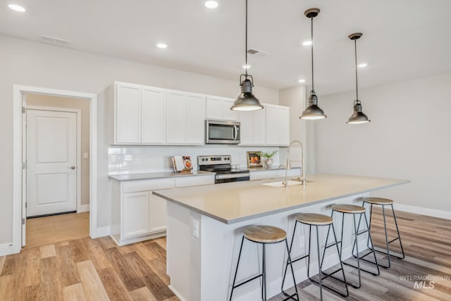 kitchen featuring white cabinets, a kitchen island with sink, pendant lighting, and appliances with stainless steel finishes