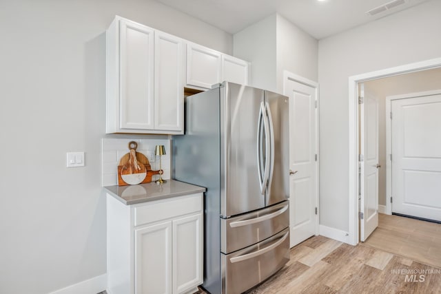 kitchen with light hardwood / wood-style floors, white cabinetry, backsplash, and stainless steel refrigerator