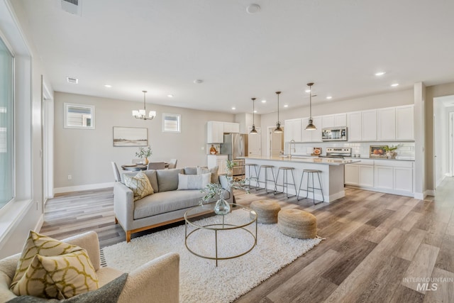 living room with sink, light hardwood / wood-style flooring, a chandelier, and plenty of natural light