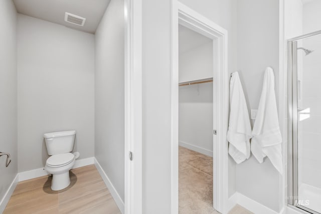 bathroom with toilet, a shower with shower door, and hardwood / wood-style flooring