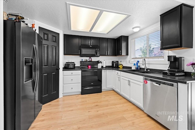 kitchen with dark countertops, a sink, black appliances, dark cabinetry, and light wood-style flooring