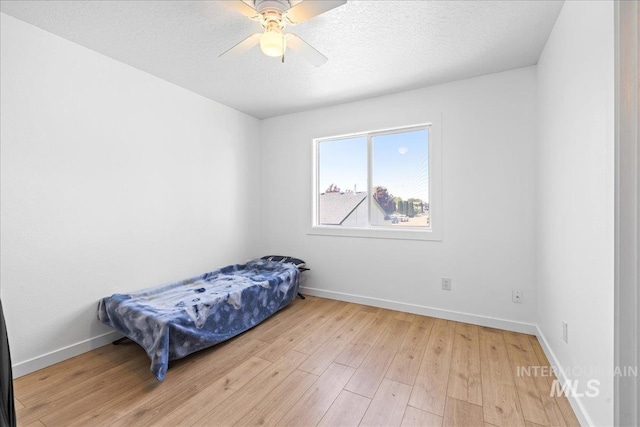 bedroom with light wood-style floors, a ceiling fan, baseboards, and a textured ceiling