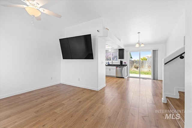 unfurnished living room with baseboards, a sink, light wood-style flooring, and stairway