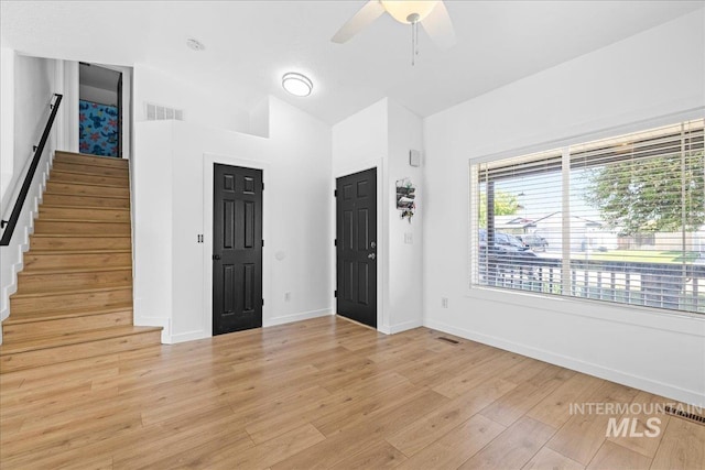 foyer entrance featuring visible vents, baseboards, stairway, light wood-type flooring, and a ceiling fan