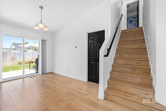 stairs with a notable chandelier, a textured ceiling, baseboards, wood finished floors, and vaulted ceiling