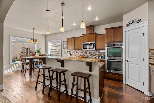 kitchen featuring a breakfast bar, dark hardwood / wood-style floors, decorative light fixtures, light stone counters, and stainless steel appliances