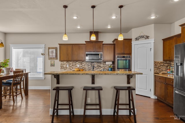 kitchen featuring light stone countertops, appliances with stainless steel finishes, dark hardwood / wood-style flooring, and pendant lighting