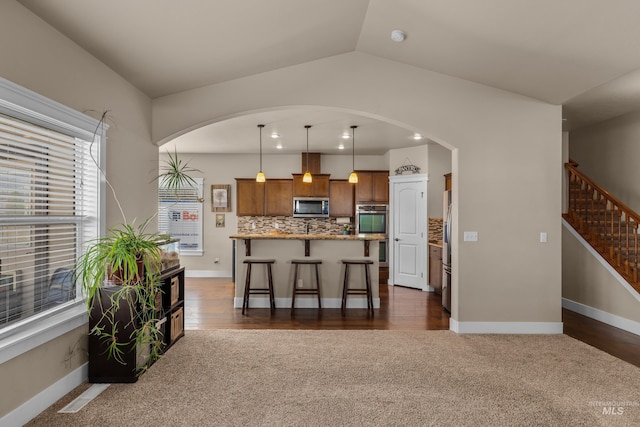 kitchen with pendant lighting, lofted ceiling, dark wood-type flooring, appliances with stainless steel finishes, and a breakfast bar area