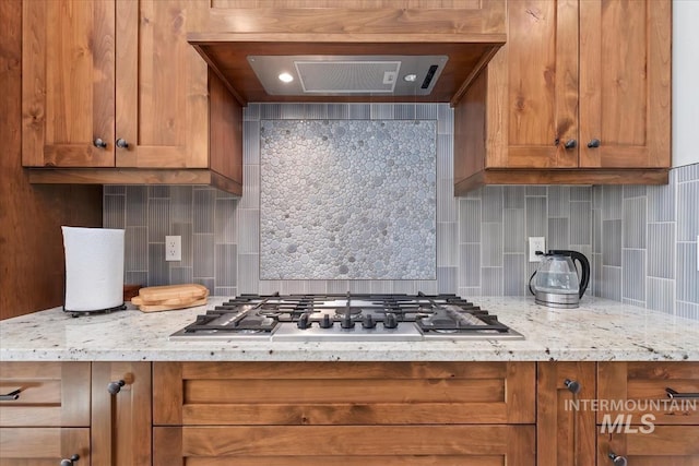 kitchen featuring stainless steel gas stovetop, custom exhaust hood, backsplash, and light stone counters