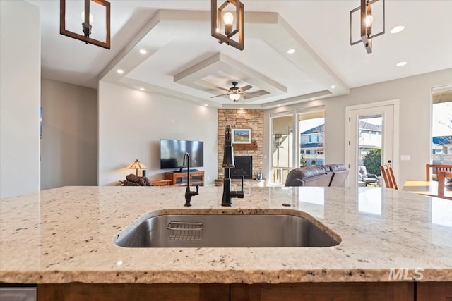 kitchen featuring pendant lighting, a fireplace, sink, light stone counters, and a tray ceiling