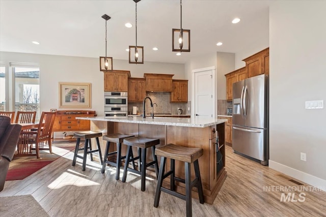 kitchen with a breakfast bar area, appliances with stainless steel finishes, a spacious island, decorative backsplash, and decorative light fixtures