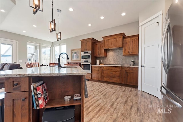 kitchen with pendant lighting, sink, stainless steel appliances, a spacious island, and light stone counters