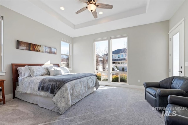 carpeted bedroom featuring multiple windows, a tray ceiling, and ceiling fan